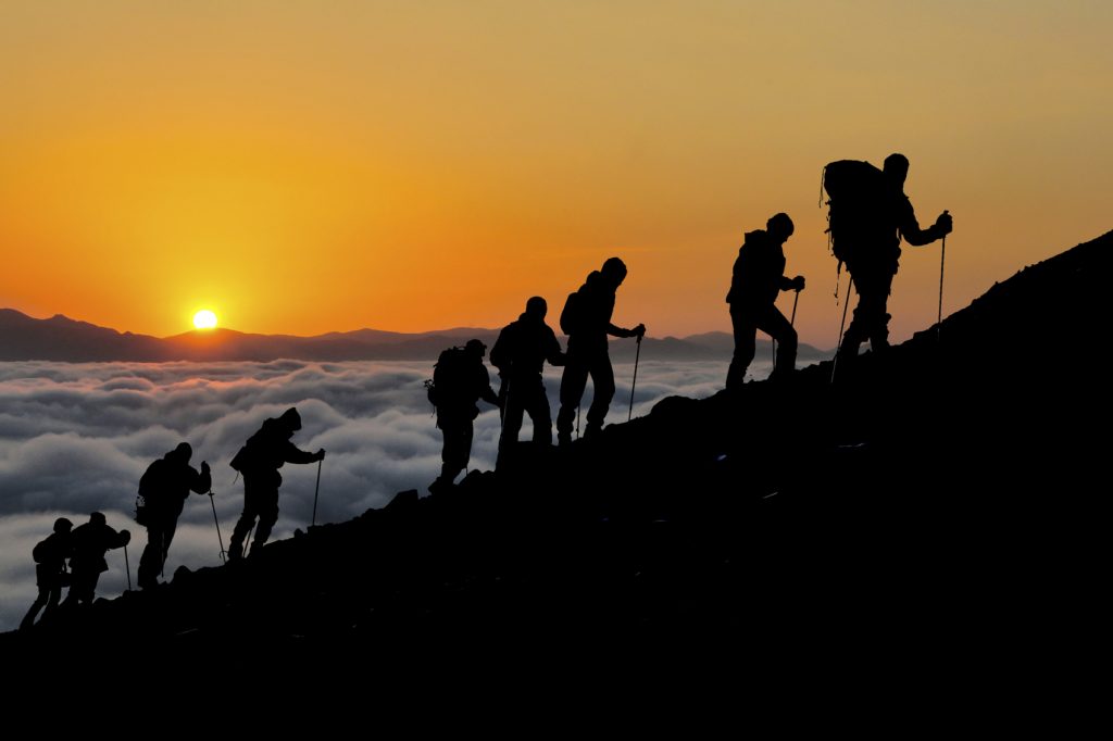 Silhouettes of hikers climbing the mountain at sunset.